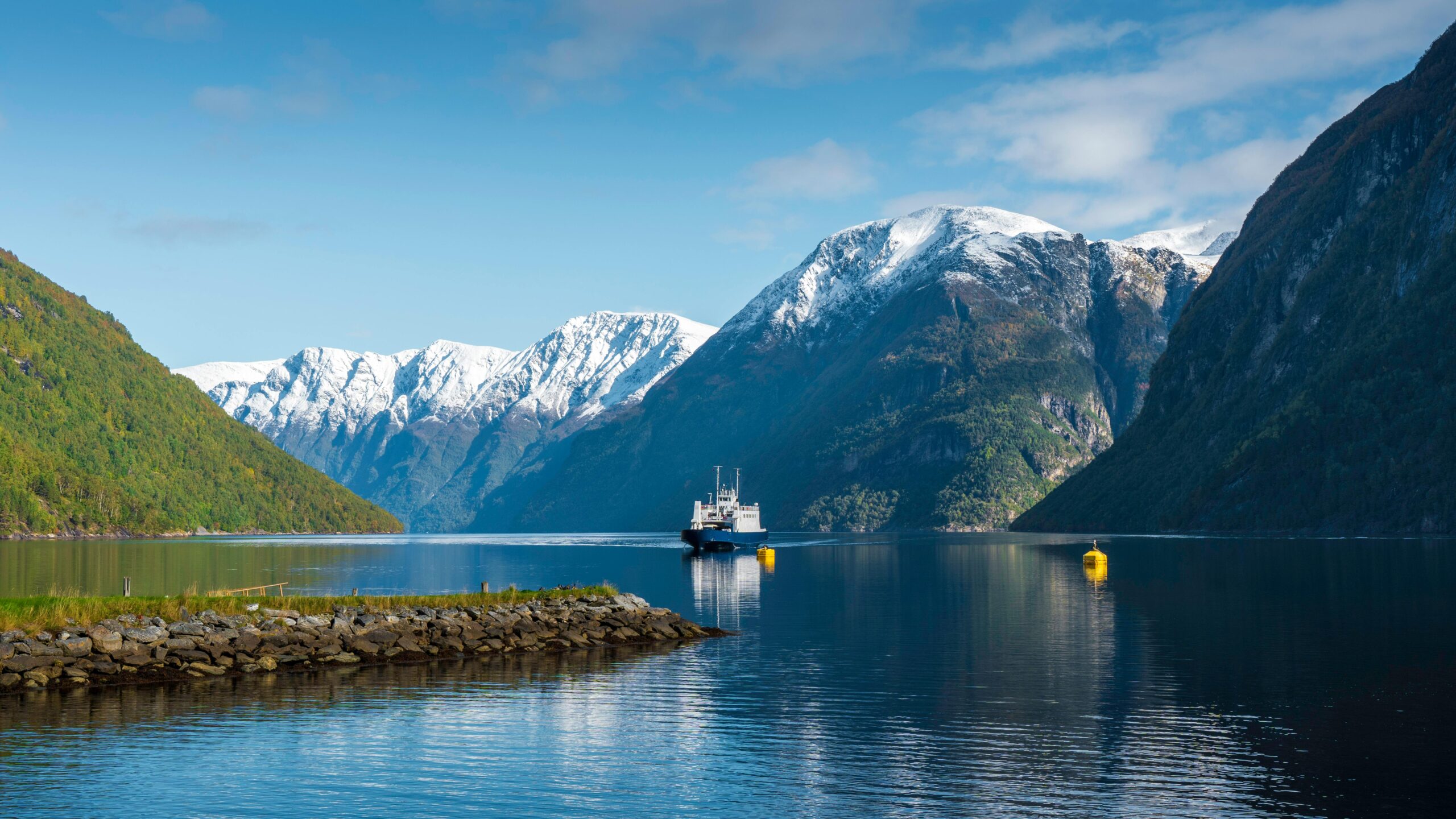 Reflective ferry traversing a stunning Norwegian fjord surrounded by snow-capped mountains.